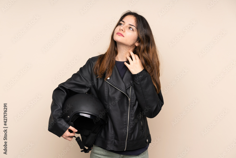 Woman with a motorcycle helmet isolated on beige background thinking an idea Woman with a motorcycle helmet isolated on beige background thinking an idea