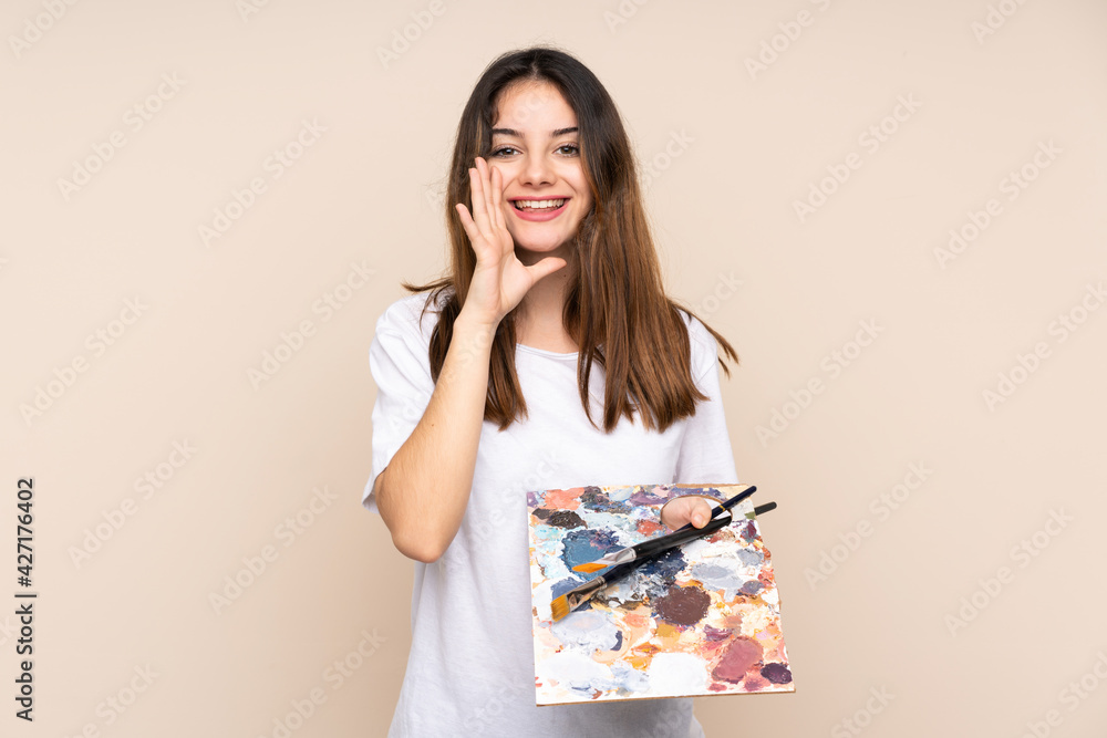 Young artist man holding a palette isolated on beige background shouting with mouth wide open Young artist man holding a palette isolated on beige background shouting with mouth wide open