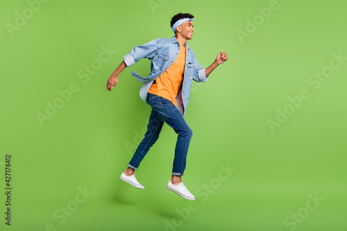 Profile photo of guy jump run look empty space wear headband jeans shirt footwear isolated green color background