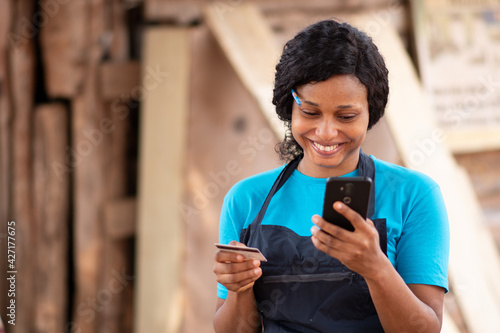 african carpenter smiling while using her credit card online with her phone