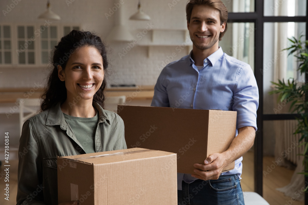 Head shot portrait happy couple tenants carrying boxes with belongings, moving day concept, smiling wife and husband relocating to first new own apartment, standing at home, mortgage or rent Head shot portrait happy couple tenants carrying boxes with belongings, moving day concept, smiling wife and husband relocating to first new own apartment, standing at home, mortgage or rent