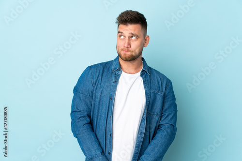 Russian handsome man isolated on blue background having doubts while looking up