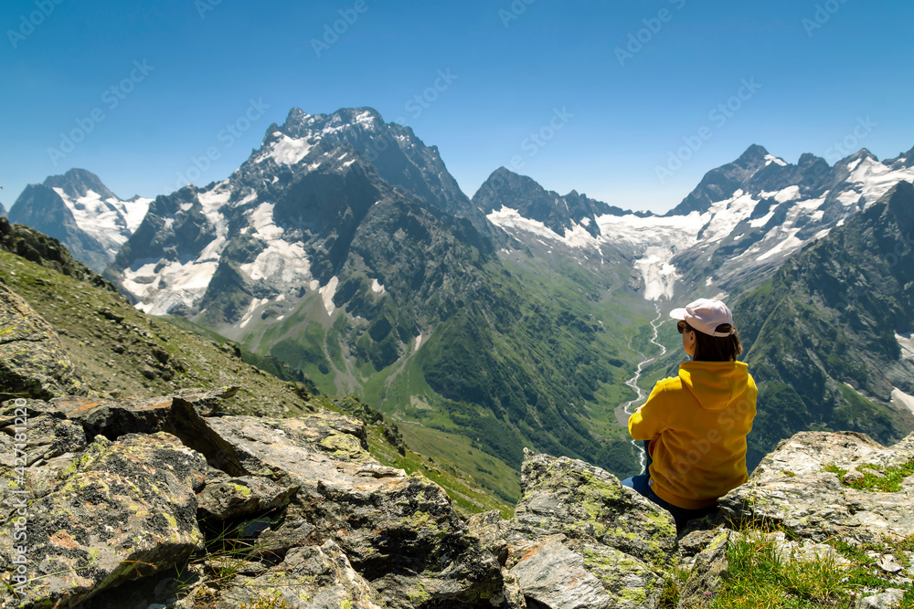 A girl on the edge of a cliff admires the mountain peaks