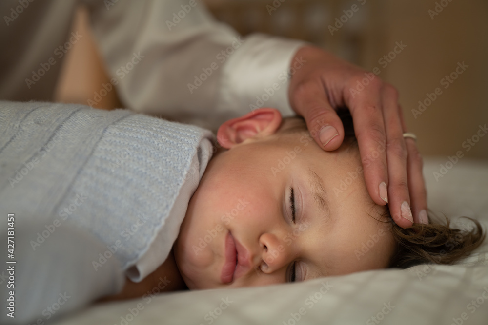 Authentic close up of mother is caressing her toddler baby boy while sleeping by day in crib with soft blanket in a nursery. Concept of family, comfort,care, love, sweet dreams, motherhood, childhood.