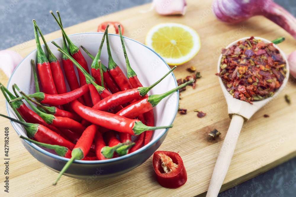red chilli pods in bowl with spices and ingredients lie on wooden chopping board, close-up red chilli pods in bowl with spices and ingredients lie on wooden chopping board, close-up