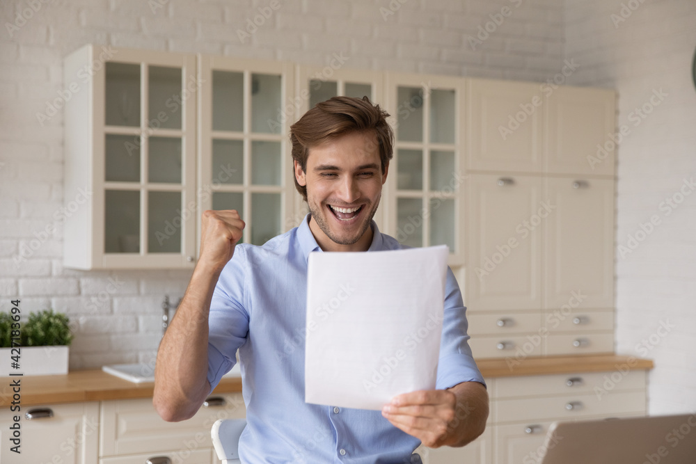Overjoyed euphoric man reading good news in letter at home, celebrating rejoicing success, amazed young male received job promotion, money refund, loan approval, excited student get scholarship Overjoyed euphoric man reading good news in letter at home, celebrating rejoicing success, amazed young male received job promotion, money refund, loan approval, excited student get scholarship