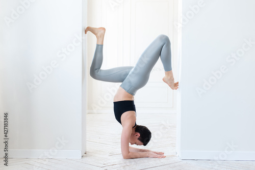 Beautiful young fitness blogger doing a difficult handstand in the light room. Concept of regular training and willpower