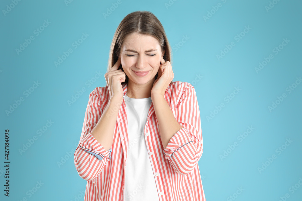 Emotional young woman covering her ears with fingers on light blue background Emotional young woman covering her ears with fingers on light blue background