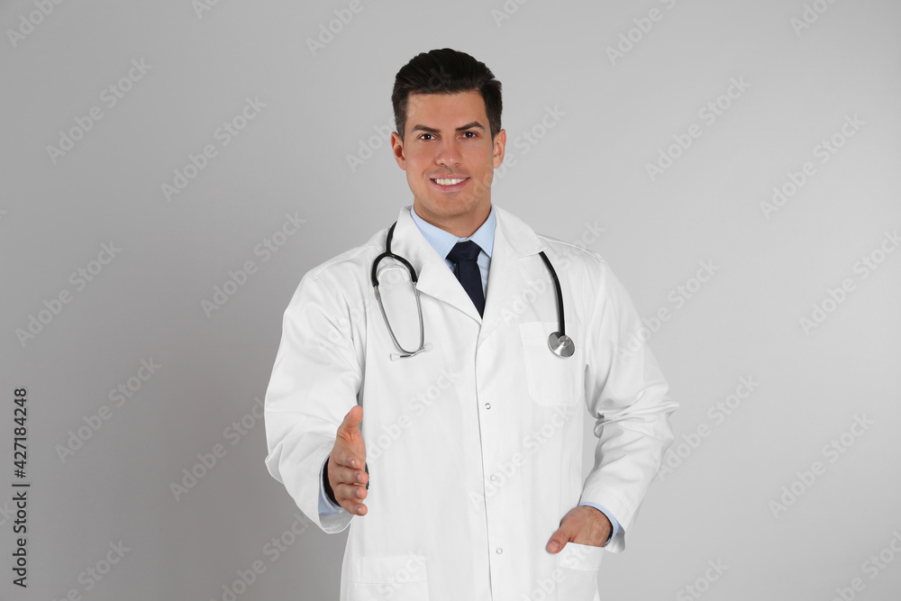 Happy male doctor offering handshake on light grey background Happy male doctor offering handshake on light grey background