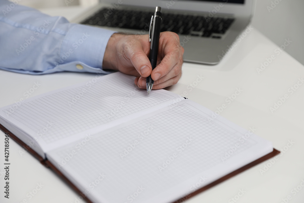 Left-handed man writing in notebook at white table, closeup Left-handed man writing in notebook at white table, closeup