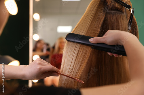 Stylist straightening woman's hair with flat iron in salon