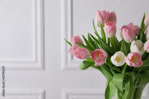 Beautiful bouquet of tulips in glass vase against white wall. Space for text