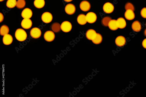 Blurred view of festive lights on black background, space for text. Bokeh effect