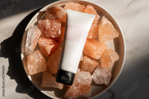 Unbranded tube with body care cosmetics lies on crystals of pink himalayan salt. Spa and wellnes concept