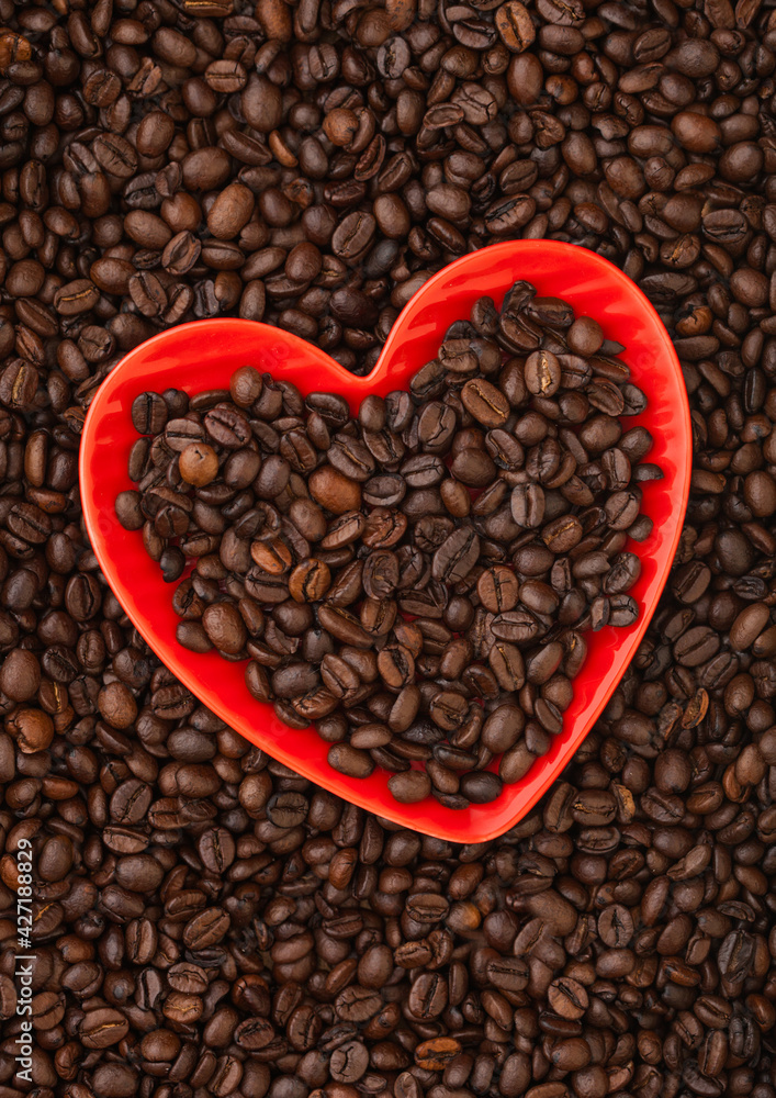 Fresh roasted coffee beans in red heart shape plate on fresh coffee beans background. Fresh roasted coffee beans in red heart shape plate on fresh coffee beans background.