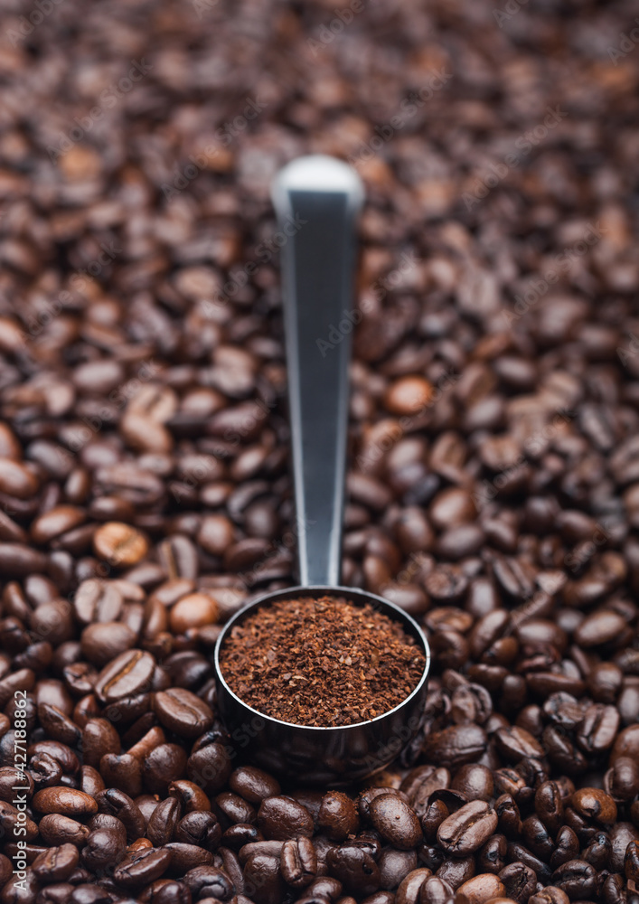 Fresh raw organic coffee powder in silver steel scoop on top of coffee beans. Fresh raw organic coffee powder in silver steel scoop on top of coffee beans.
