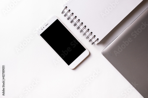 Close laptop on a white background next to a mobile phone and a ring notebook.