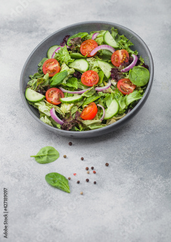 Grey bowl in motion with healthy fresh vegetables salad with lettuce and tomatoes, red onion and spinach on light background.