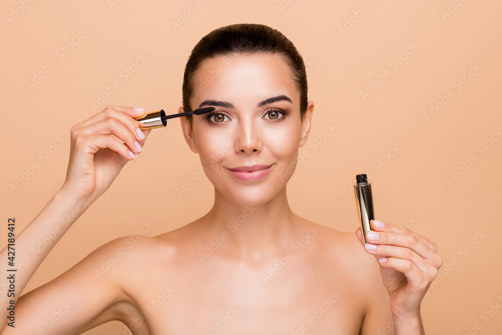 Photo of optimistic brunette hairdo apply mascara without clothes isolated on pastel beige color background Photo of optimistic brunette hairdo apply mascara without clothes isolated on pastel beige color background