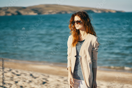 woman on the sand on the beach near the sea in a coat travel tourism sunglasses