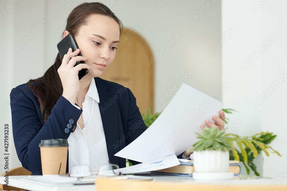 Young businesswoman making phone call to discuss details of agreement with colleague Young businesswoman making phone call to discuss details of agreement with colleague