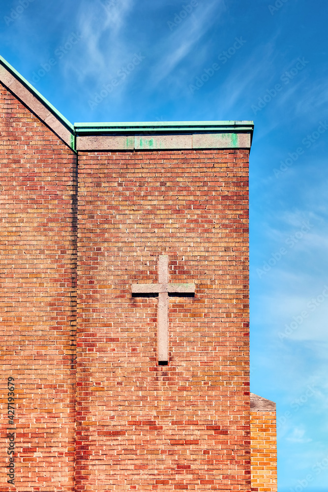 Cross symbol on the exterior brick wall of a church building.