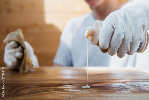 A girl in work gloves pours oil on a wooden tabletop. Coating wood with oil photo