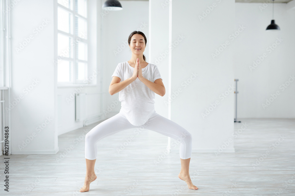 Asian pregnant female performing prenatal Goddess or Sumo Squat Pose Asian pregnant female performing prenatal Goddess or Sumo Squat Pose