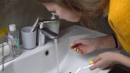 The image of a pretty woman, brushing her teeth, rinsing her mouth with water. The tap is turned on and in front of the sink, she takes a mouthful of water and rinses it, then spits it out.