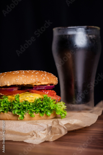 Homemade burger and french fries with oregano and frozen glass a tasty soda. Humburger served on pergament paper and wooden board. Close up.