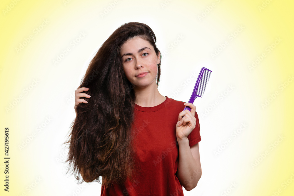 Portrait of a young caucasian woman holding her thick dark hair and comb for combing. White and yellow background. Copy space. Hair care concept Portrait of a young caucasian woman holding her thick dark hair and comb for combing. White and yellow background. Copy space. Hair care concept