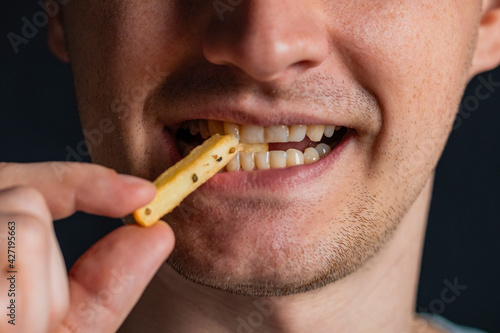 Young man bites fries. Extreme close up. Guy eats eating fried potatoes, isolated. Male mouth.