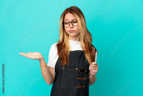 Young hairdresser girl over isolated blue background holding copyspace with doubts