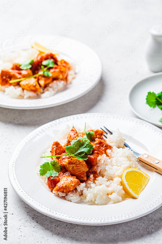 Fried chicken in tomato sauce with rice on white plate, gray background. Fried chicken in tomato sauce with rice on white plate, gray background.