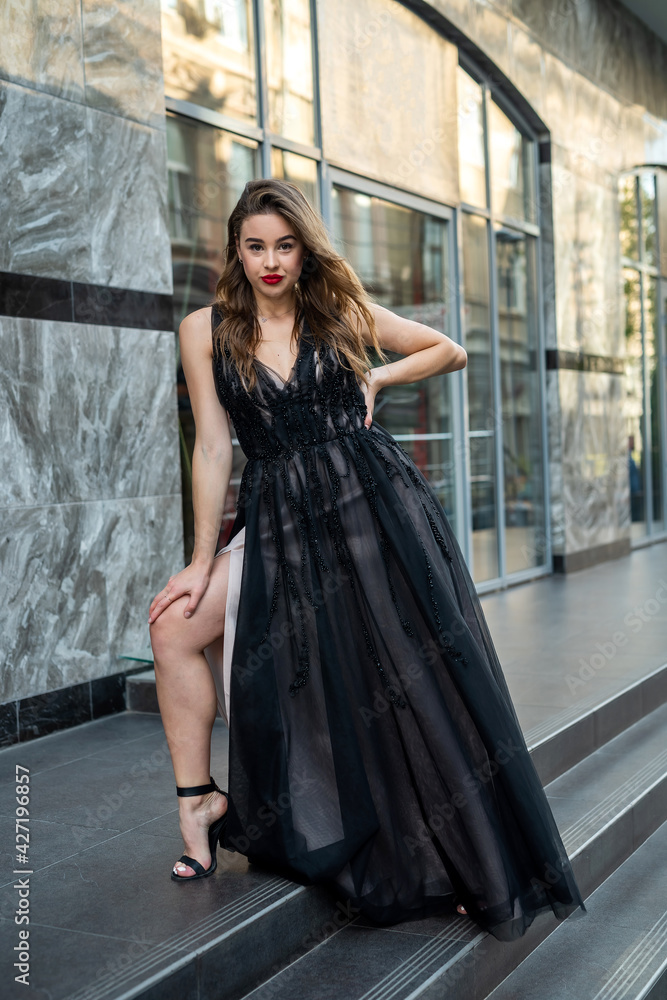 portrait of attractive female model in gorgeous evening black dress posing in street of city