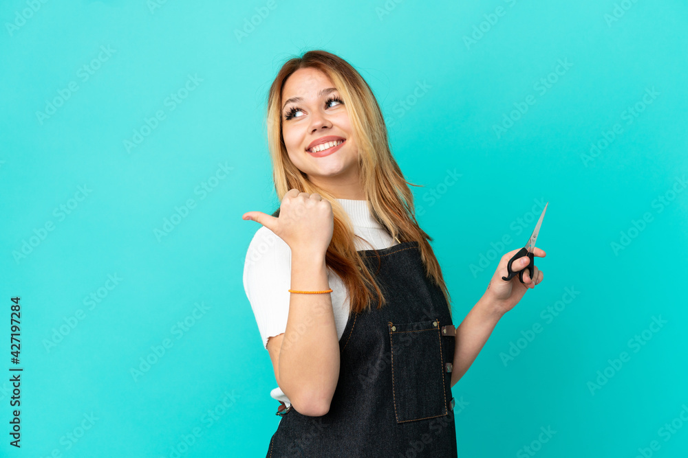 Fototapeta premium Young hairdresser girl over isolated blue background pointing to the side to present a product
