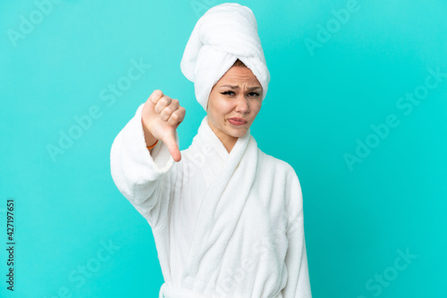 Teenager blonde girl in a bathrobe over isolated blue background showing thumb down with negative expression