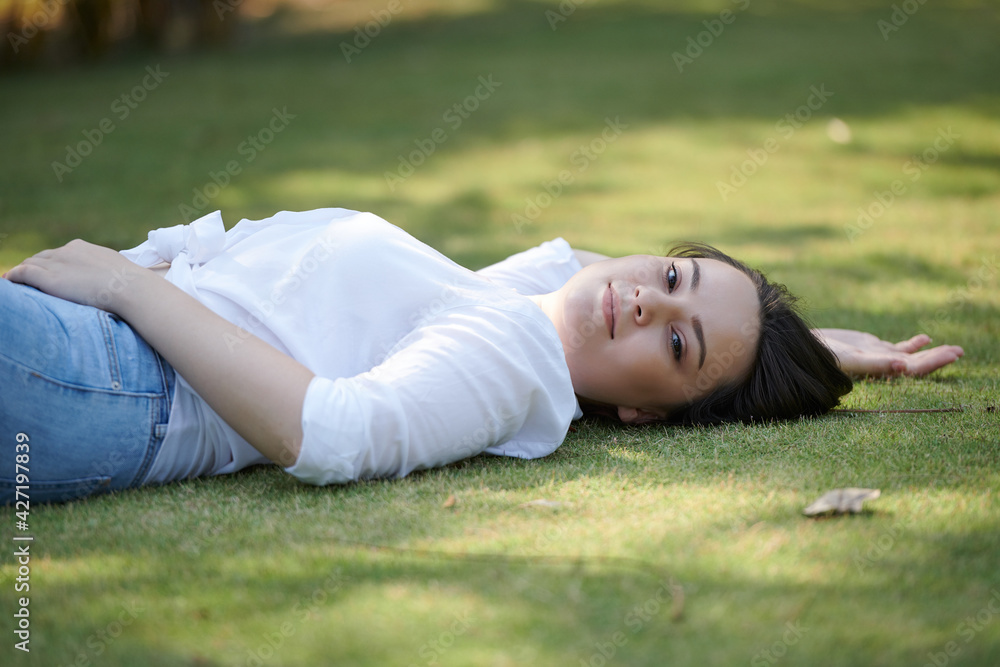 Beautiful smiling young woman lying on ground in park an looking at camera Beautiful smiling young woman lying on ground in park an looking at camera