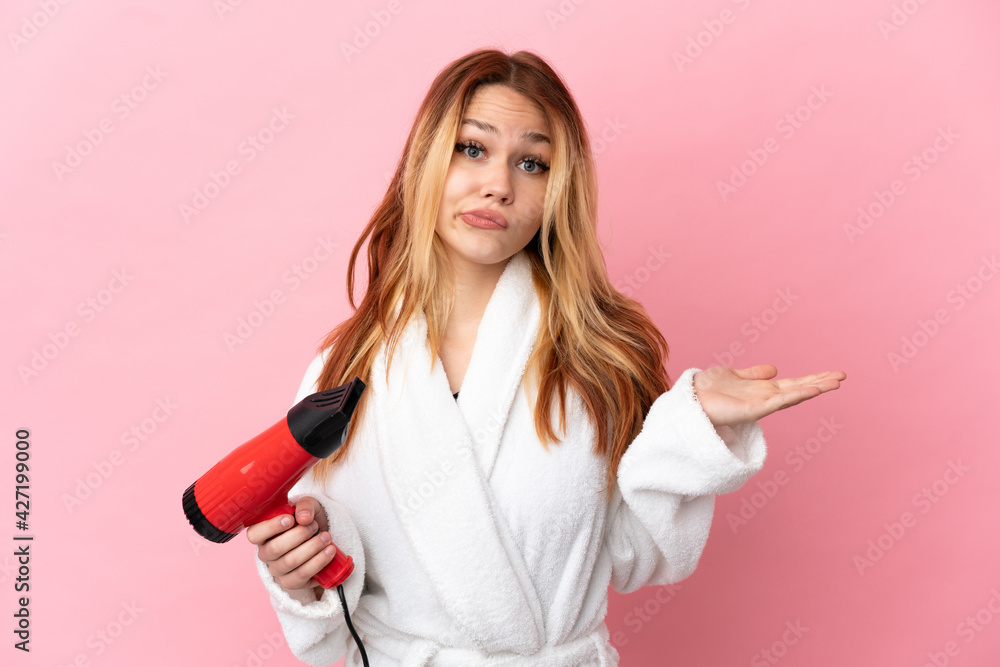 Teenager blonde girl holding a hairdryer over isolated pink background having doubts while raising hands Teenager blonde girl holding a hairdryer over isolated pink background having doubts while raising hands