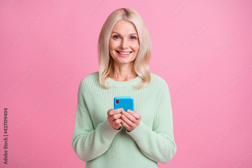 Photo portrait of positive old lady holding phone in two hands isolated on pastel pink colored background Photo portrait of positive old lady holding phone in two hands isolated on pastel pink colored background