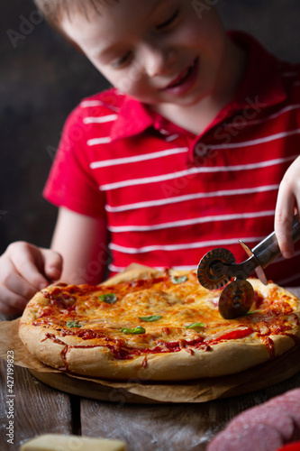 Child cuts a round pizza with a pizza knife