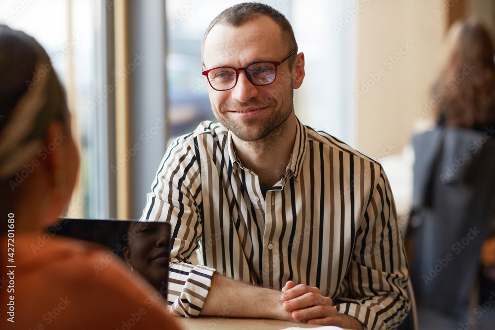 Fototapeta premium Portrait of smiling adult man looking at partner while enjoying business meeting at cafe table, copy space