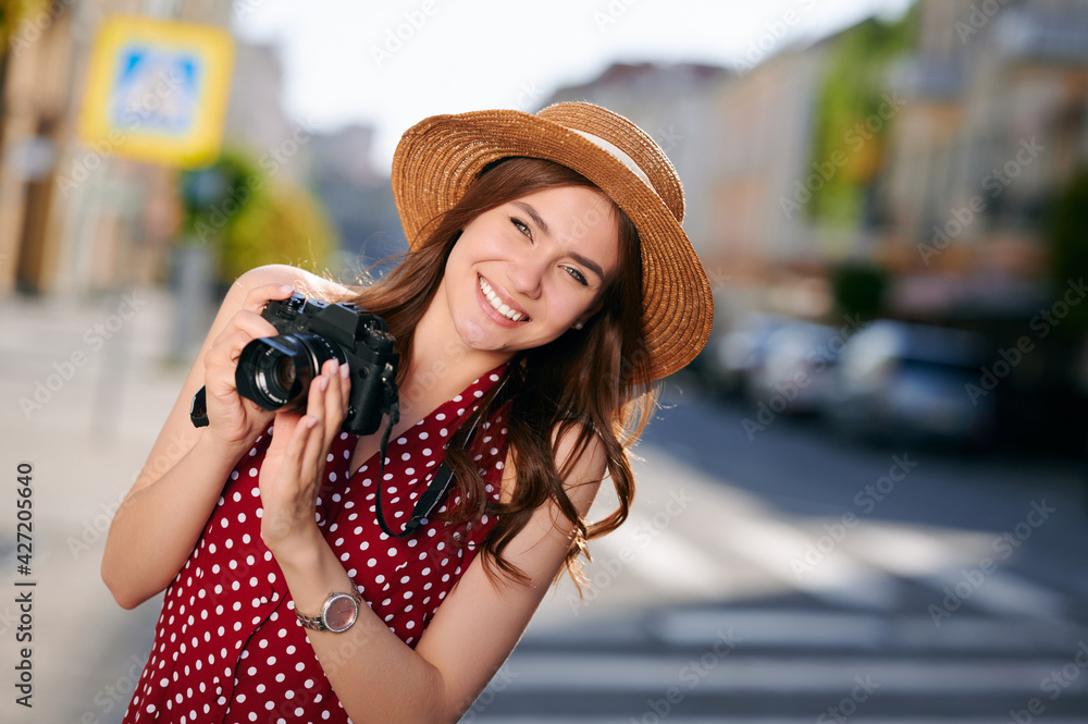 Stylish female traveler spending holiday trip on hobby taking photos of urban standing on street. Woman photographer using camera for making picture of city architecture