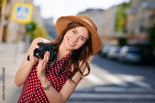 Stylish female traveler spending holiday trip on hobby taking photos of urban standing on street. Woman photographer using camera for making picture of city architecture © khmelev