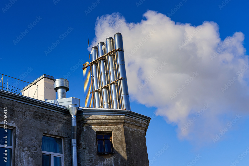 Many chimneys on the roof of an old house smoke against a blue sky Many chimneys on the roof of an old house smoke against a blue sky