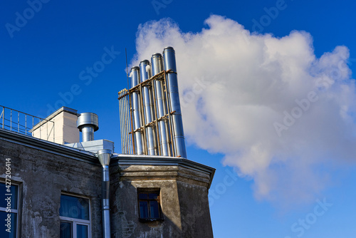 Many chimneys on the roof of an old house smoke against a blue sky