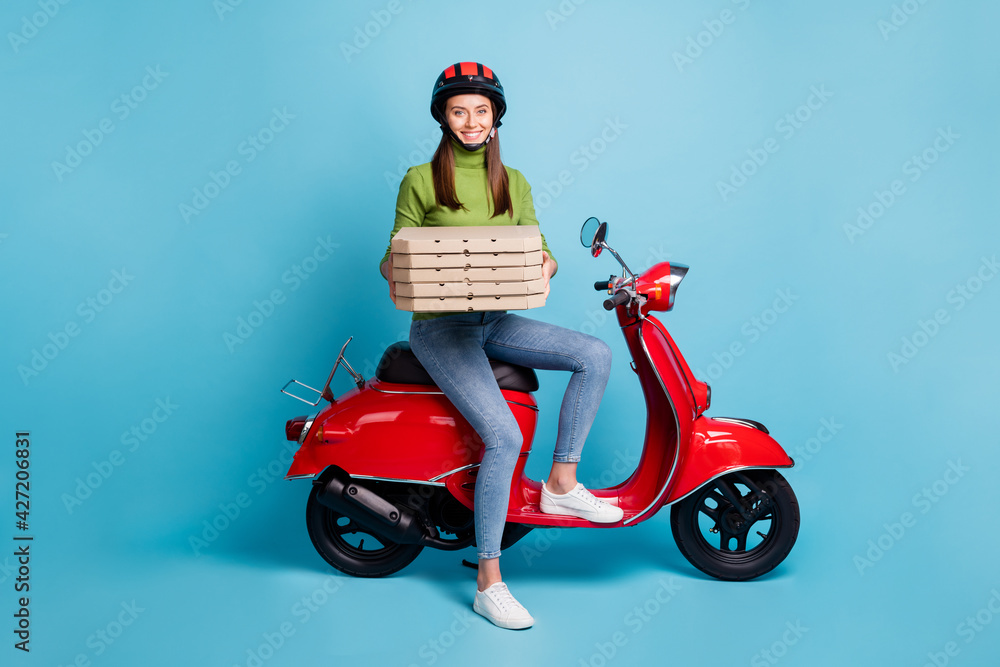 Full length photo portrait of woman holding stacked pizza boxes sitting on red scooter isolated on pastel blue colored background Full length photo portrait of woman holding stacked pizza boxes sitting on red scooter isolated on pastel blue colored background