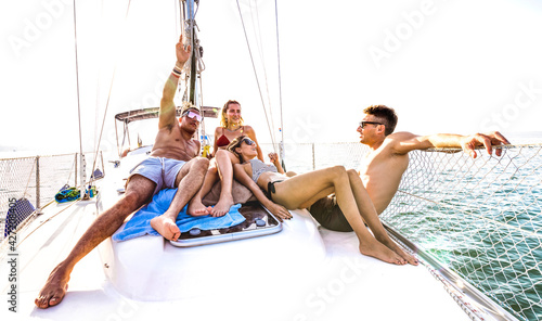 Front view of young millennial friends chilling on sailboat at sea ocean trip - Guys and girls having summer fun together at sail boat party day - Luxury excursion concept on bright vivid filter