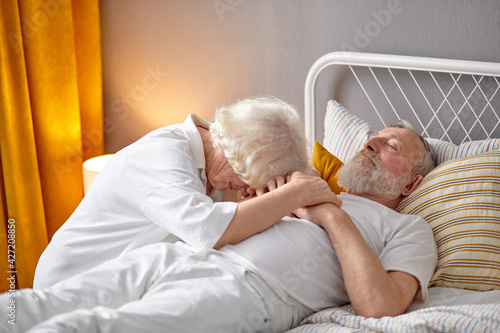 Tableau sur toile Senior woman sitting next to dying husband lying on bed and crying