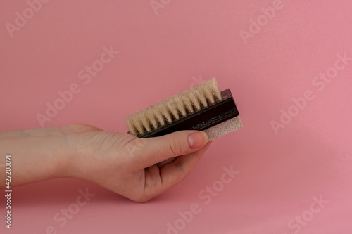 Brush with stone scrub foot hygiene tool in a woman's hand on pink background